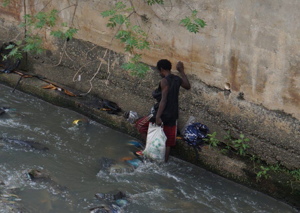 Homem procurando alimento em um valão — Foto: Bruno Assunção (O Canal)